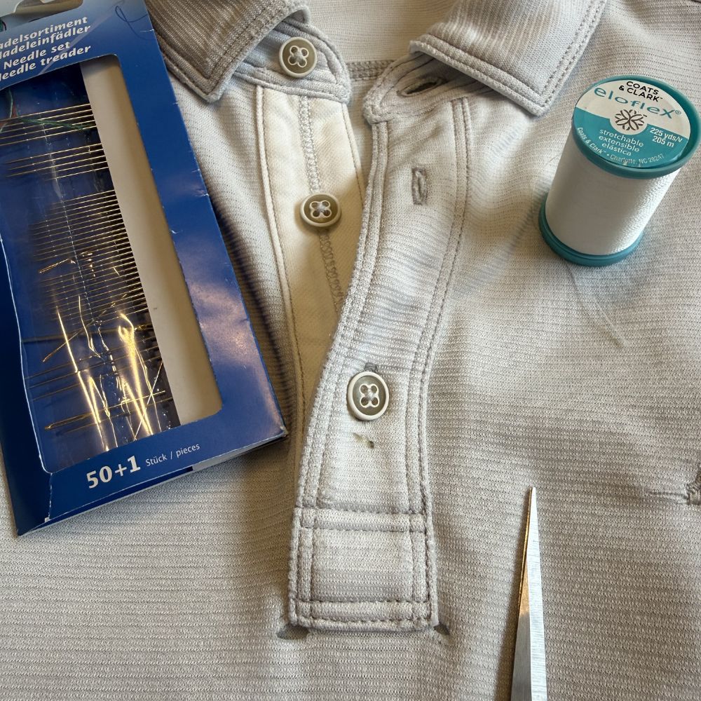 Two small holes at the top of a grey knit polo placket, needle and stretch thread ready