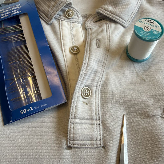Two small holes at the top of a grey knit polo placket, needle and stretch thread ready