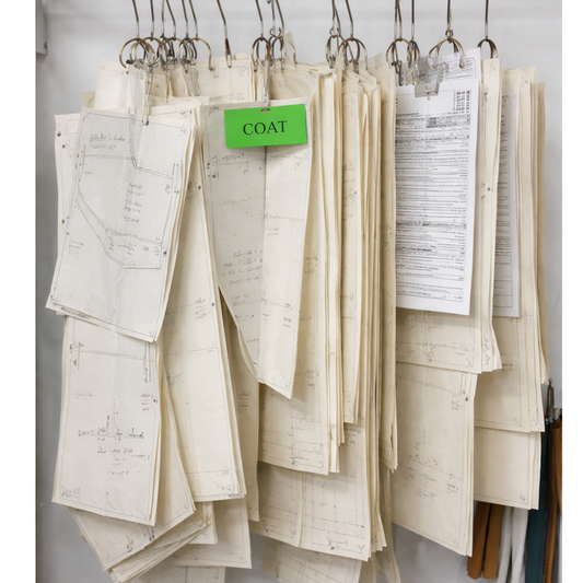 Professional pattern making workspace with drafted coat pattern pieces, tailor's notes, and technical specifications for garment production