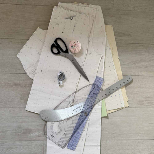 Paper pattern pieces, fabric shears and a curved ruler laid out on the floor.