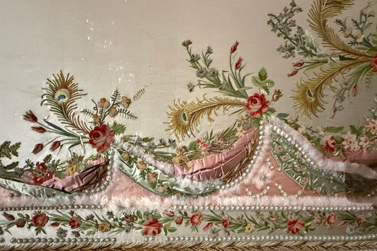 Close-up of an elaborately embroidered 18th century bodice with silk roses, peacock feathers, and pearl trim — Marie Antoinette exhibition, London