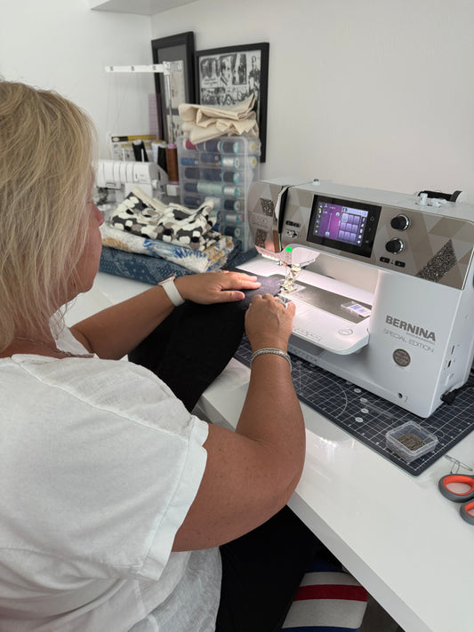 sewing at a Bernina machine in her home sewing studio, surrounded by fabric and thread