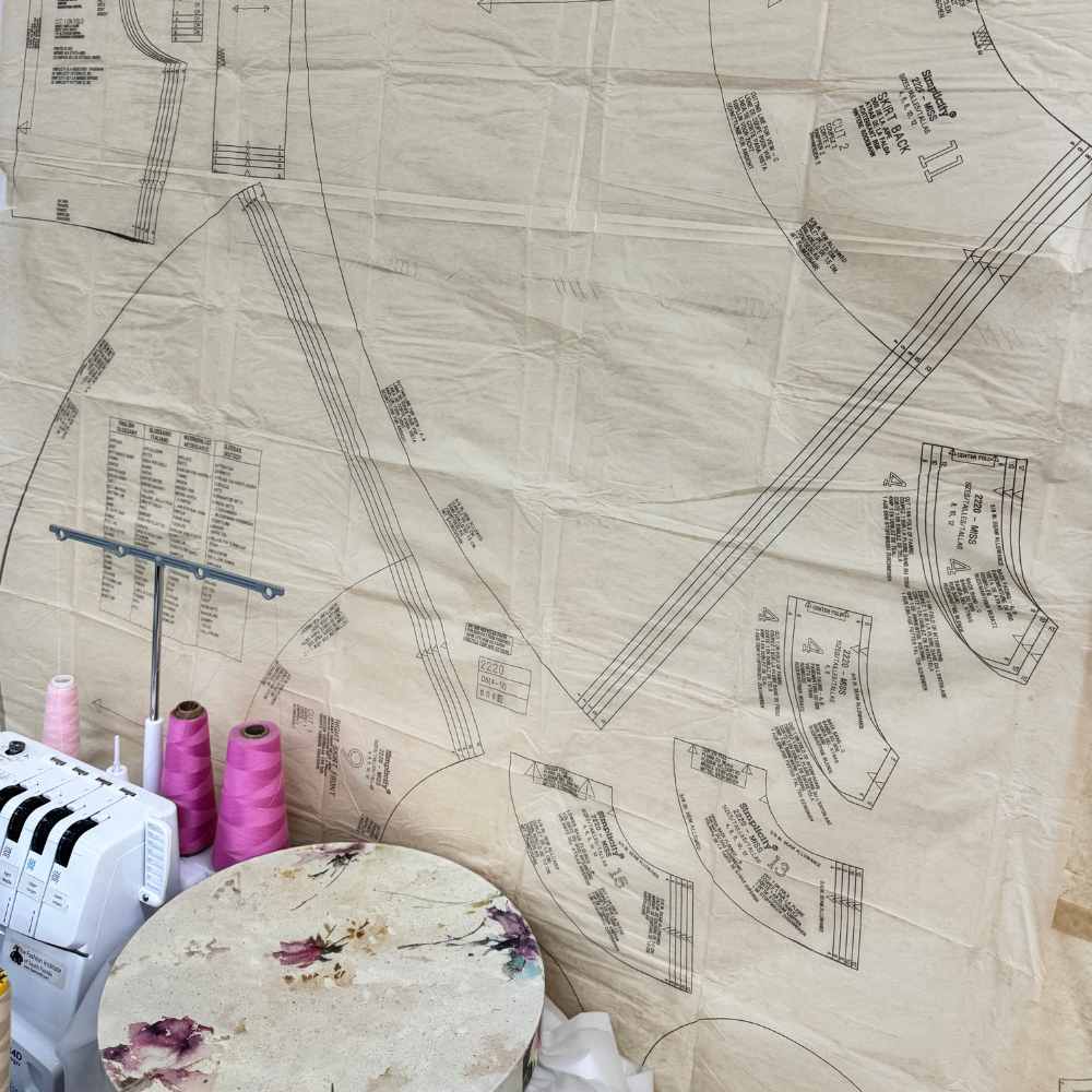 Hand-drafted pattern pieces spread across a work table with thread and a machine.