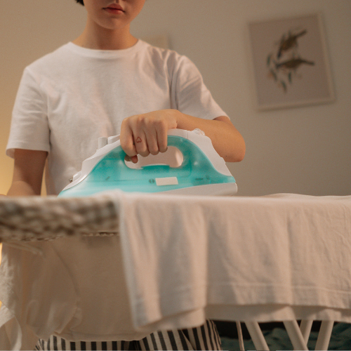 Person ironing everyday clothing, representing thoughtful garment care and maintenance