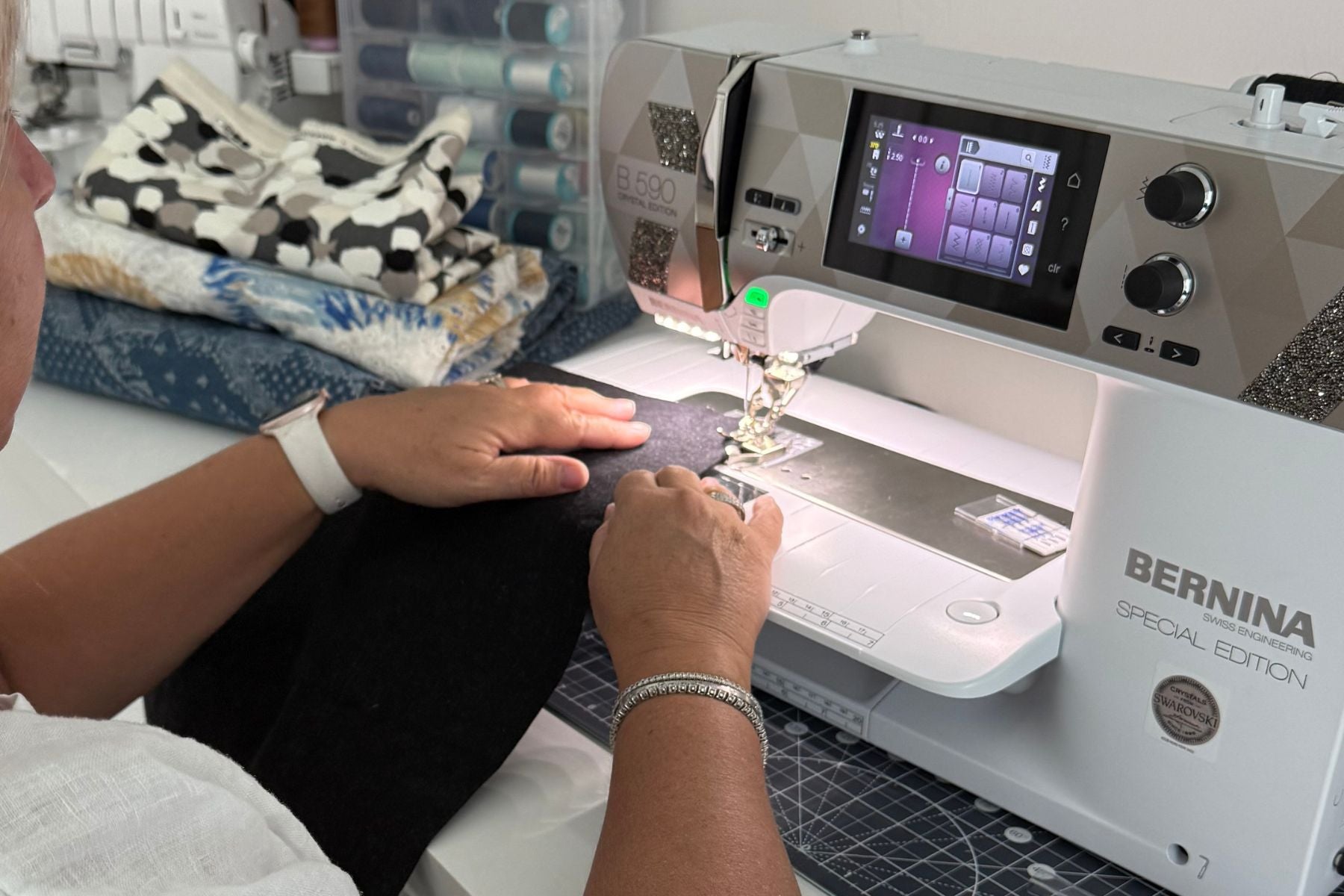 Nicola sewing at a Bernina machine in her home sewing studio, surrounded by fabric and thread