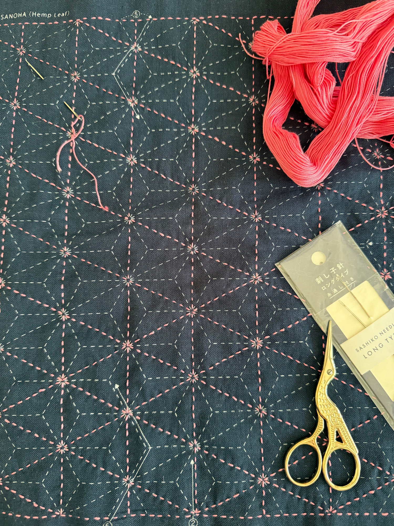 Sashiko Japanese Embroidery Sampler with pink thread and scissors on a dark blue background