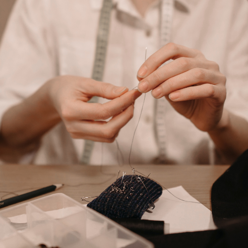 Hand sewing needle and thread on fabric, clothing alterations as part of intentional dressing.
