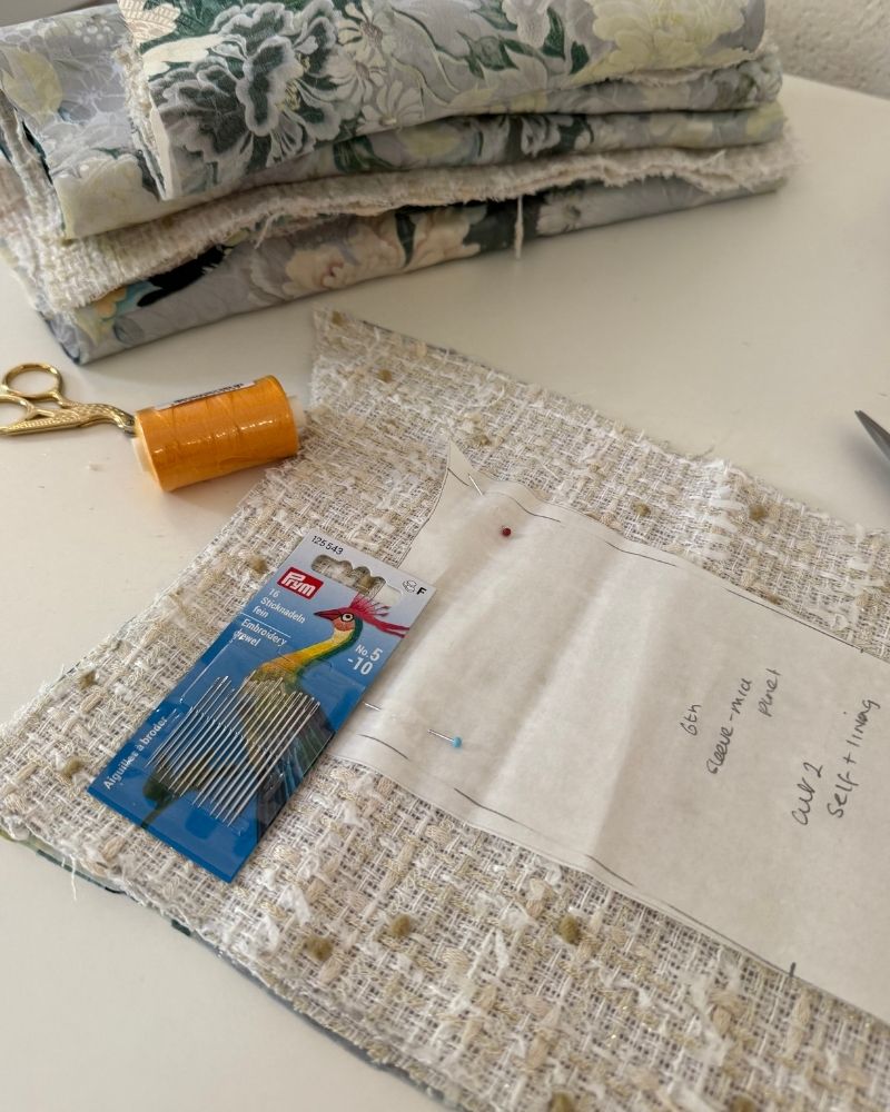 French couture jacket in progress — tweed fabric, pattern pieces, embroidery needles and thread on the atelier table — After Stilettos