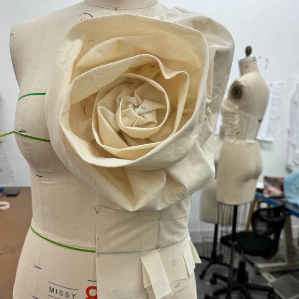 Fabric draping technique on dress form creating sculptural rose-inspired design element