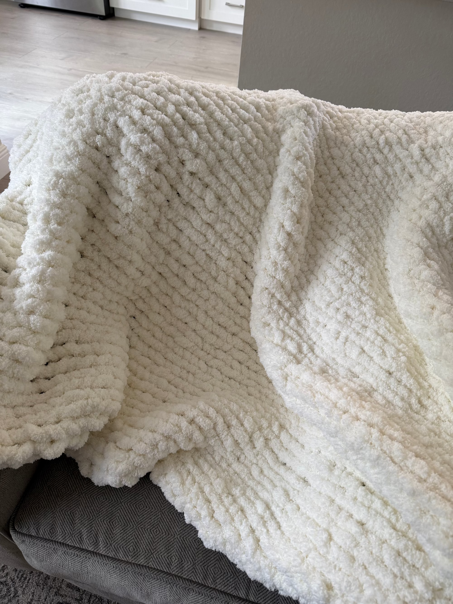 Cream-colored chunky finger-knitted blanket draped over a sofa in a neutral living room