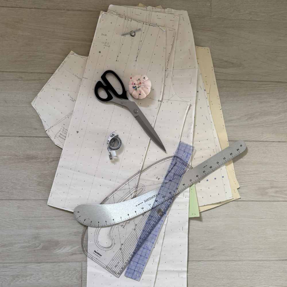 Paper pattern pieces, fabric shears and a curved ruler laid out on the floor.
