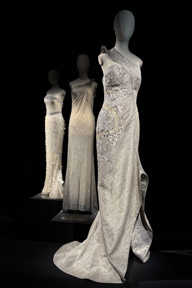 Three silver crystal and beaded one-shoulder gowns on mannequins displayed at the Giorgio Armani Privé 2005–2025 retrospective, Milan 2025
