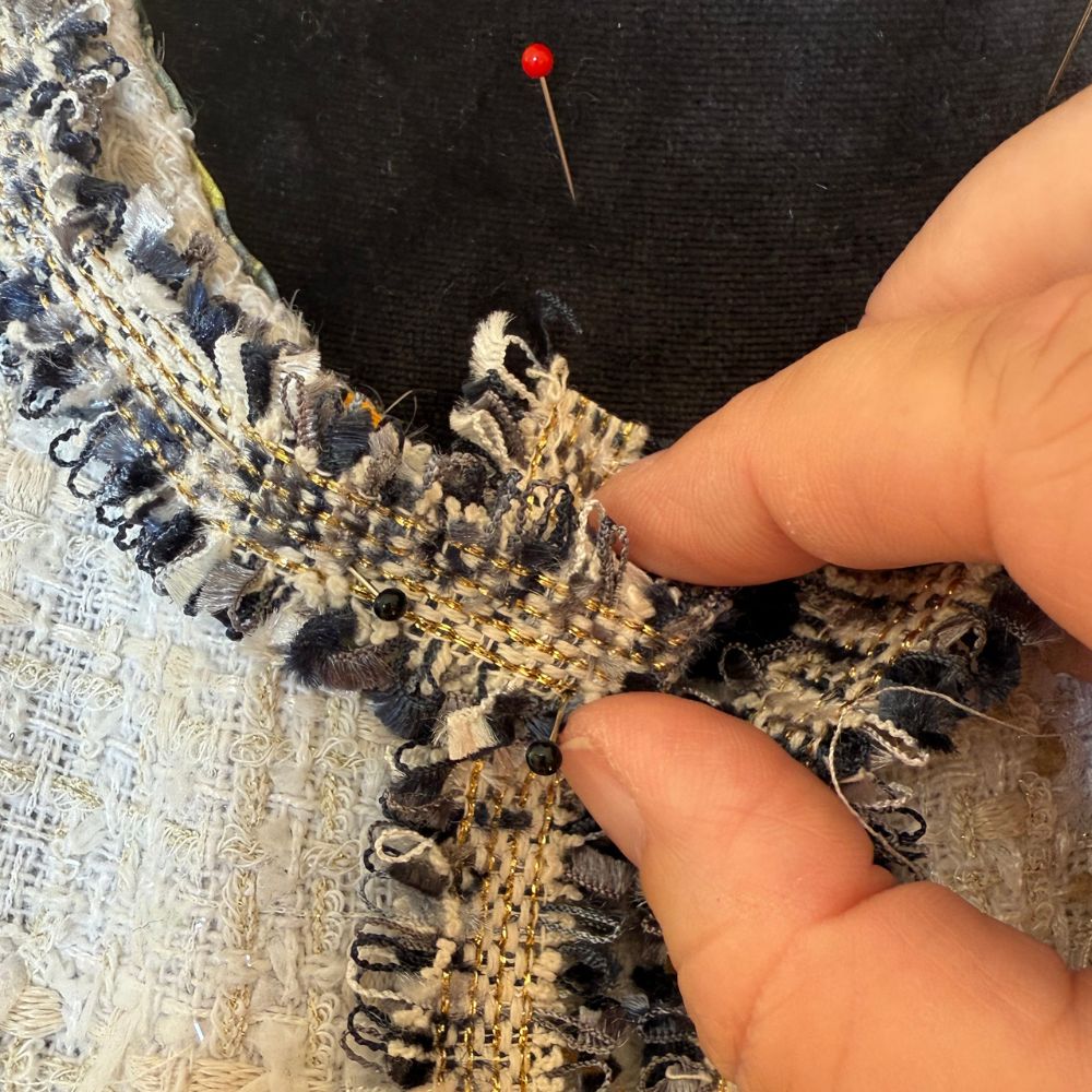 Close-up of hands working the raw edge of navy and gold tweed fabric pinned to a dress form — After Stilettos Making a French Couture Jacket by Hand
