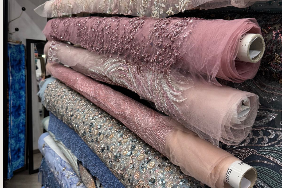 Stacked rolls of embellished tulle, beaded lace, and sequin fabric in blush, mauve, and silver tones — After Stilettos atelier