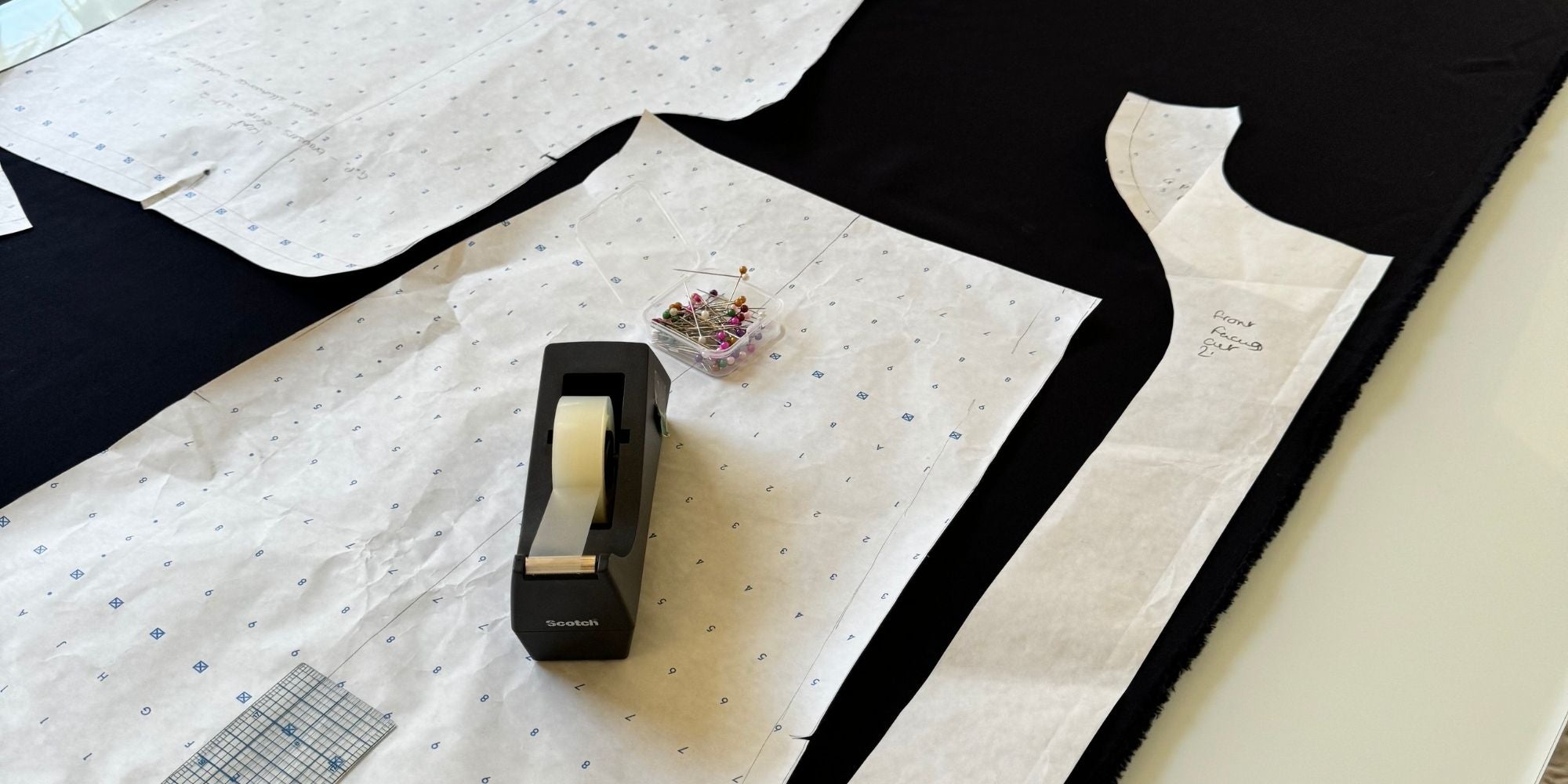 Black fabric laid out on cutting table with dressmaking pattern pieces, pins, and ruler — After Stilettos atelier process