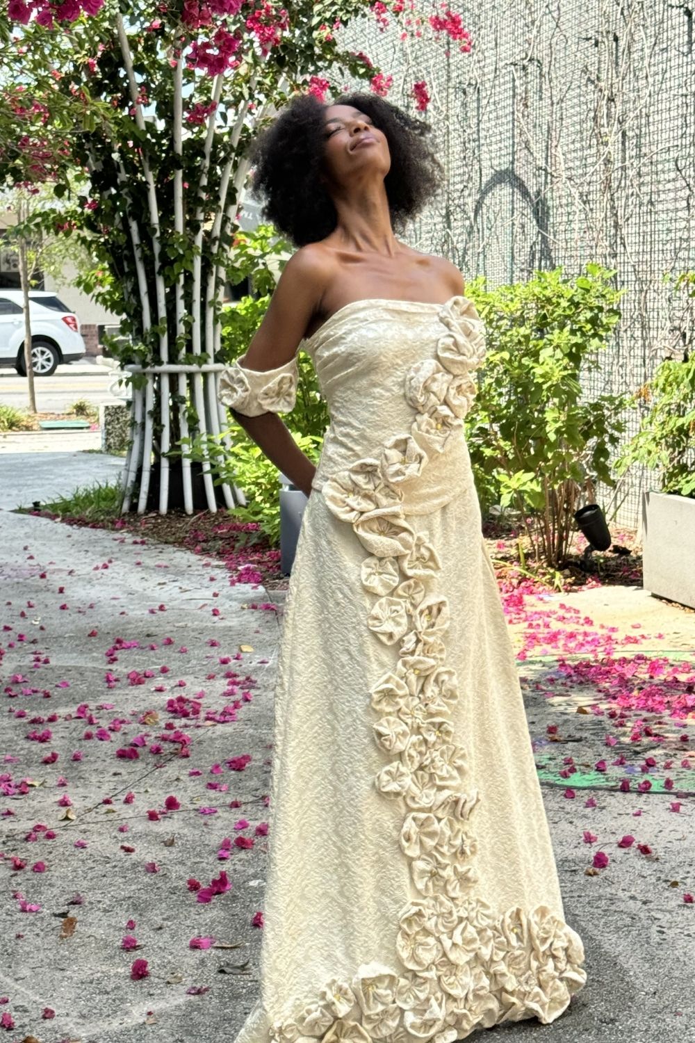 Model wearing Midnight Cascade ivory brocade off-shoulder gown with cascading sculptural roses, outdoor editorial shoot by After Stilettos