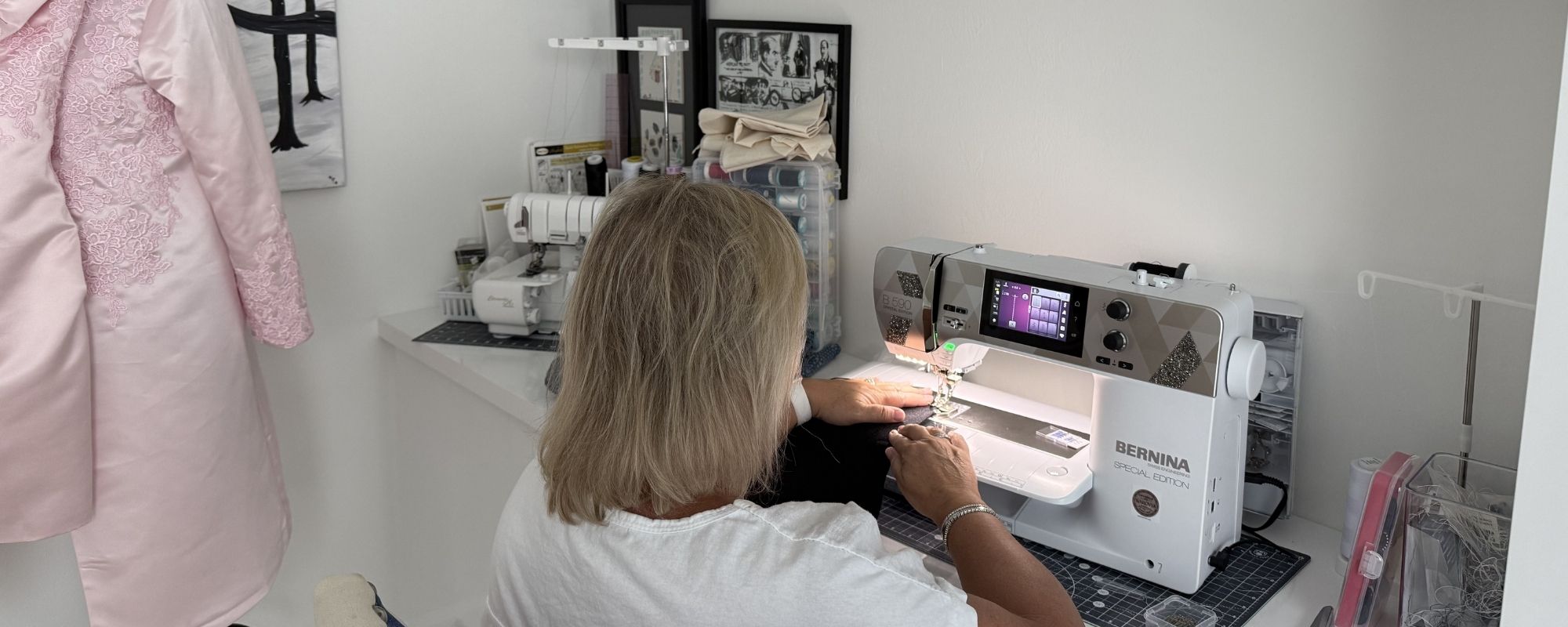 Nicola Grayling sewing at her Bernina machine in the After Stilettos atelier with a pink embellished dress in the background