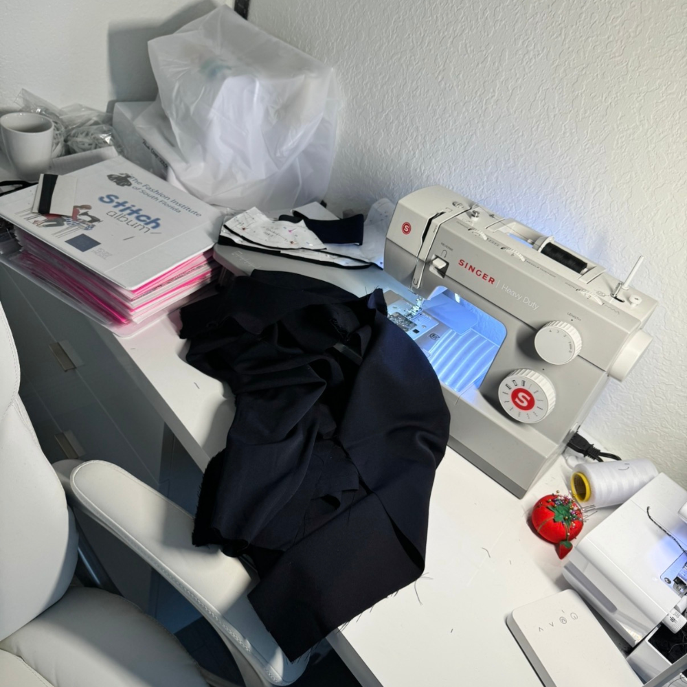 Garment in progress at a sewing workspace, featuring a Singer sewing machine, black fabric, and pattern books in a calm studio setting