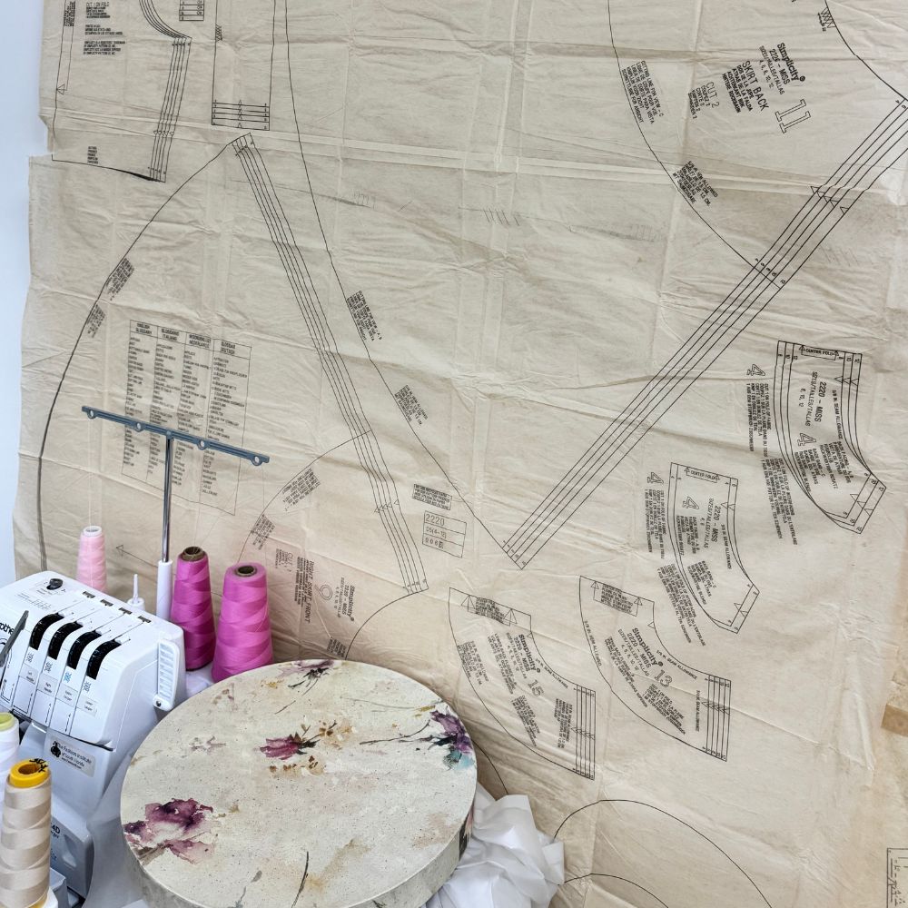 Vintage sewing pattern laid flat with serger machine and pink thread spools — After Stilettos Fashion School Diaries
